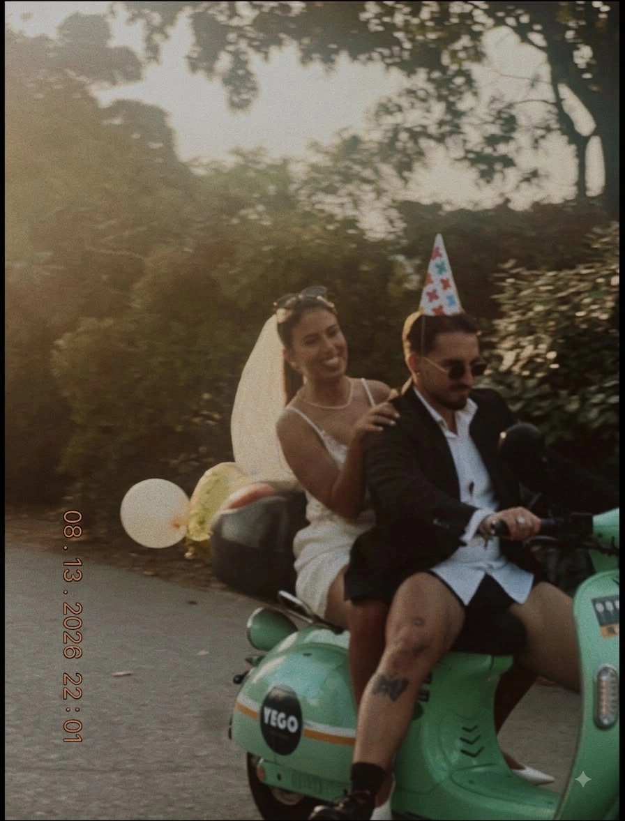 Joana, veil on, smiling behind Cristian as he rides a green scooter